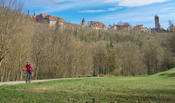 nice city woman on a cycling tour on a famous German route of castles, below the medieval skyline of Rothenburg ob der Tauber, Franconia, Bavaria, Germany - Фото, изображение