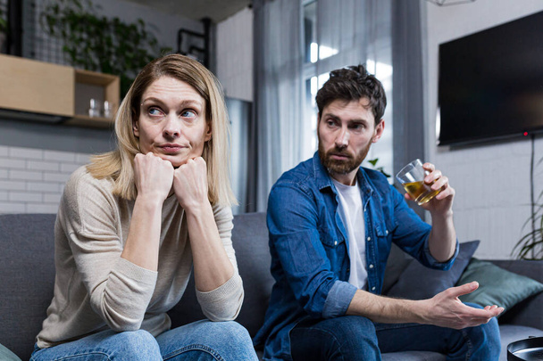 Young family falls apart, depressed woman because of alcoholic husband, couple sitting on sofa in living room - 写真・画像