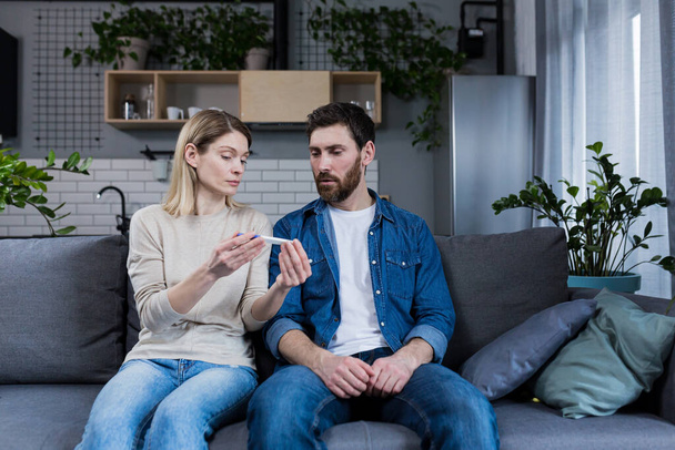 Sad man and woman sitting on the couch, disappointed with a negative pregnancy test - Foto, Imagen