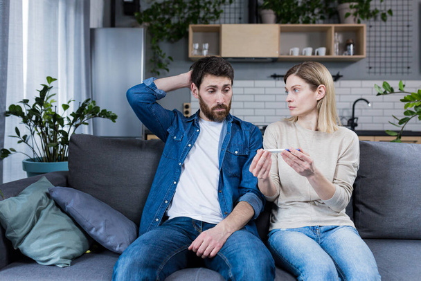 Sad man and woman sitting on the couch, disappointed with a negative pregnancy test - Fotoğraf, Görsel