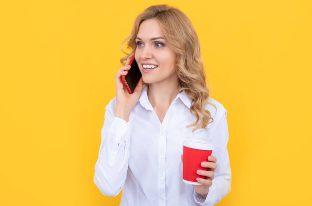 zadowolona blondynka z filiżanką kawy rozmawia przez telefon na żółtym tle - Zdjęcie, obraz
