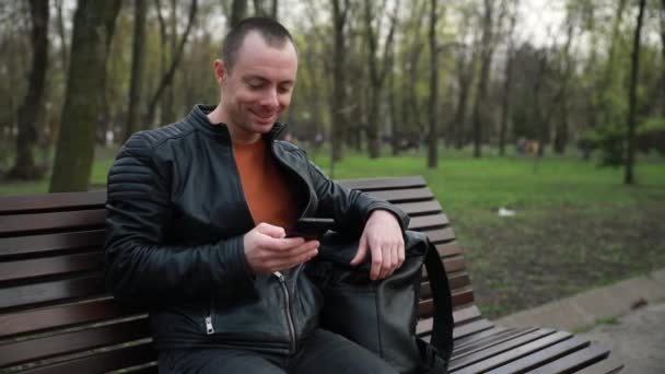 zakenman met telefoon op een bankje in een stadspark - Video