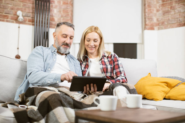 Relaxed happy mature couple using tablet on couch - Photo, image