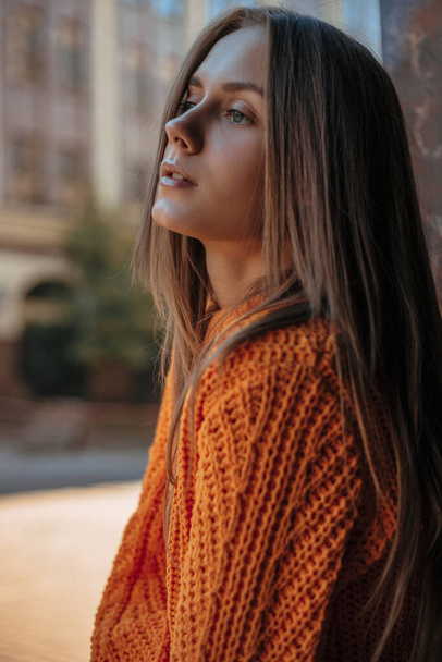 piękna blondynka stojąca na ulicy i spoglądająca w bok. Profil portret modelki ubranej w pomarańczowy sweter z dzianiny  - Zdjęcie, obraz
