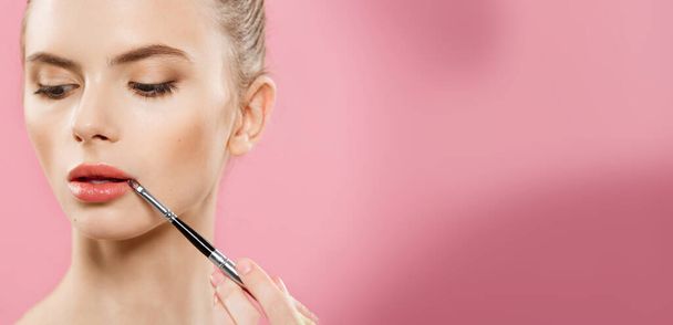 Beauty Concept - Mujer que aplica lápiz labial rojo con fondo de estudio rosa. Hermosa chica hace maquillaje
. - Foto, imagen