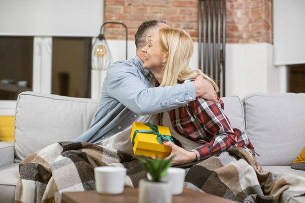 Mature couple embracing on couch and sharing with gifts - Foto, Imagen