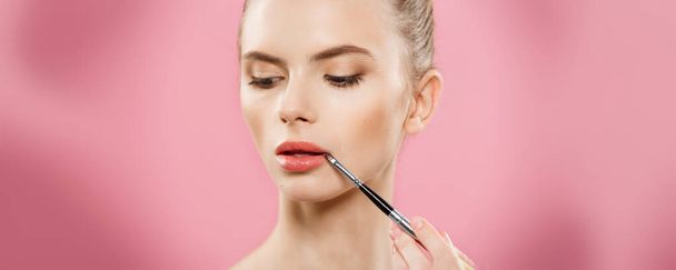 Beauty koncept - žena používat červenou rtěnku s růžové studio pozadí. Krásná dívka dělá make-up. - Fotografie, Obrázek