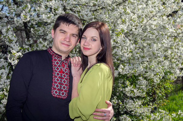 Mladý milující pár muž a žena v vyšívaných košilích v blízkosti kvetoucího stromu v jarní zahradě. - Fotografie, Obrázek