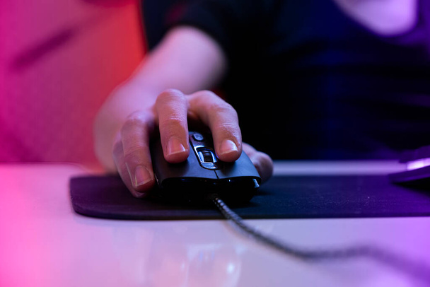 Oyuncunun eli farenin üzerinde, oyuncunun eli farenin üzerinde seçici bir odak ile fotoğrafı yakın. Sanal sporcu oyunu oynayıp fareye tıklayın. Sıcak ışıkları olan karanlık bir odada çevrimiçi oyuncu. - Fotoğraf, Görsel