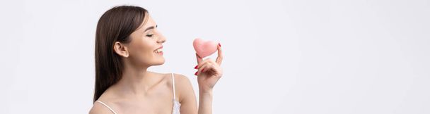 Beautiful smiling woman with clean skin, natural make-up and white teeth on a gray background. Holding a pink hygienic heart. - Photo, Image