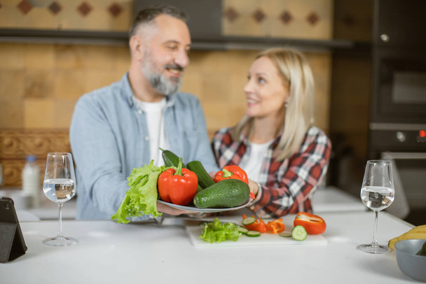 Mature couple holding healthy eco vegetable on kitchen - Фото, изображение