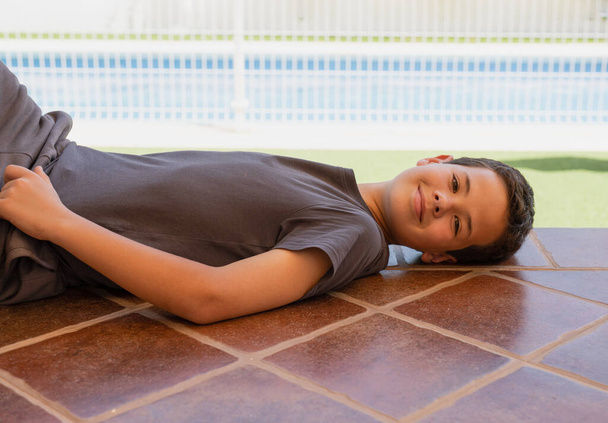Nuori onnellinen poika makaa lattialla terassilla kotona ulkona. - Valokuva, kuva