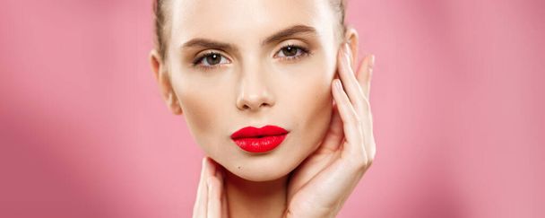 Beauty concept - Close up Gorgeous Young Brunette Woman face portrait. Beauty Model Girl with bright eyebrows, perfect make-up, red lips, touching her face. Isolated on pink background - 写真・画像