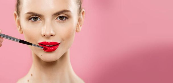 Schönheitskonzept - fröhliche kaukasische Frau mit langen Haaren und roten Lippen posiert vor rosa Studiohintergrund. - Foto, Bild