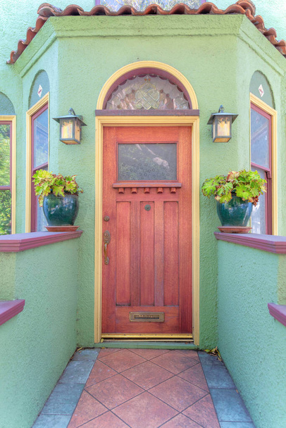 Entrance of a house with mediterranean structure and green exterior at San Francisco, California. Tiled path to the wooden front door with glass and two potted plants on the wall on both sides. - Photo, Image