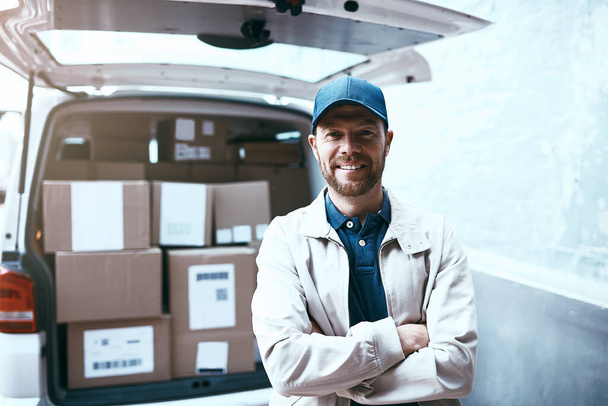 All packed up and ready for delivery. Portrait of a cheerful young delivery man standing next to a van full of boxes with his arms folded outside during the day. - Foto, imagen