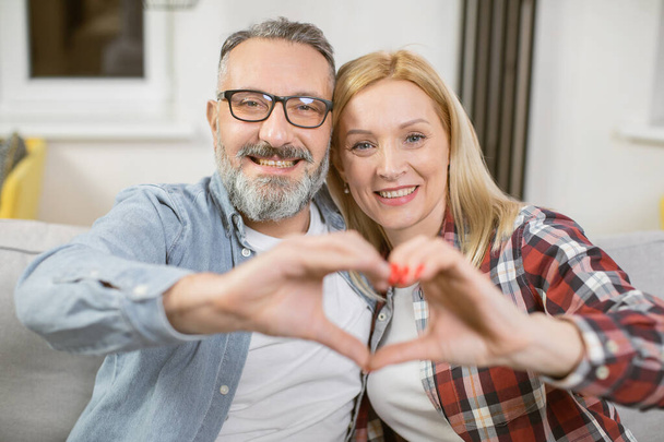 Mature couple making heart shape with hands on couch - Foto, Imagem