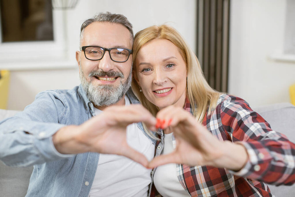 Mature couple making heart shape with hands on couch - Fotografie, Obrázek