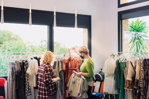 volwassen mode verkoopster adviseren van haar klanten, in kleine modewinkel. winkelconcept - Foto, afbeelding