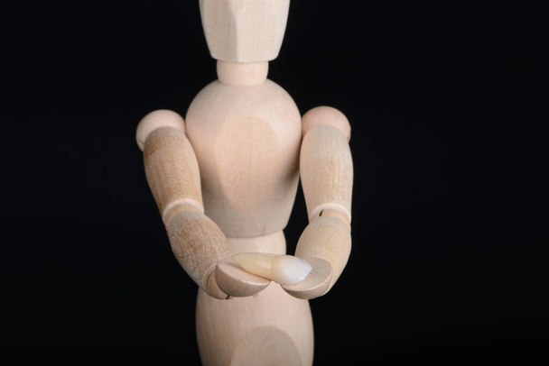 Human wooden figure holds in hands a zirconia bridge with glazour on a black background. - Фото, изображение
