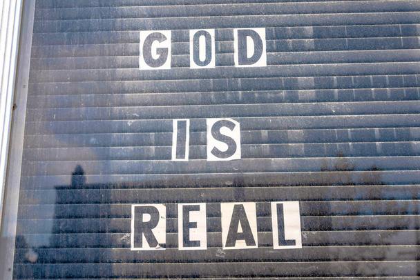 Glass window with God is real letterings on a white paper at San Francisco, California. Posted papers against the black closed window blinds. - Photo, Image