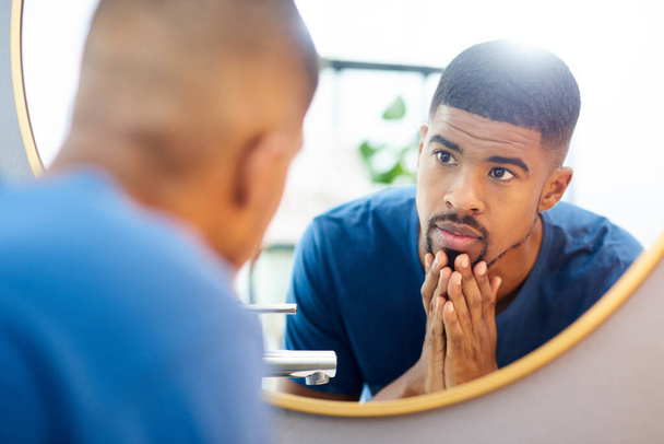 My new skincare routine has paid off. Shot of young man admiring his face in his bathroom mirror. - Photo, image