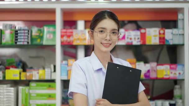 Porträt, eine schöne asiatische Apothekerin steht und lächelt selbstbewusst im Apothekenservice. - Filmmaterial, Video