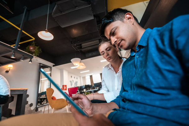Homme d'affaires multiethnique avec une collègue féminine travaillant ensemble sur tablette informatique dans un espace de détente du bureau de démarrage moderne - Photo, image