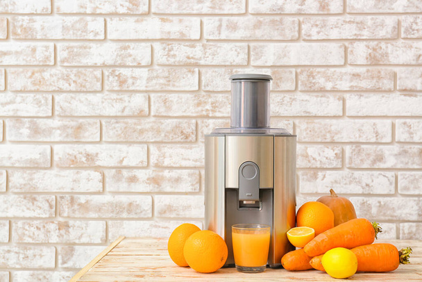 New modern juicer and glass of fresh juice on light wooden table - Фото, изображение
