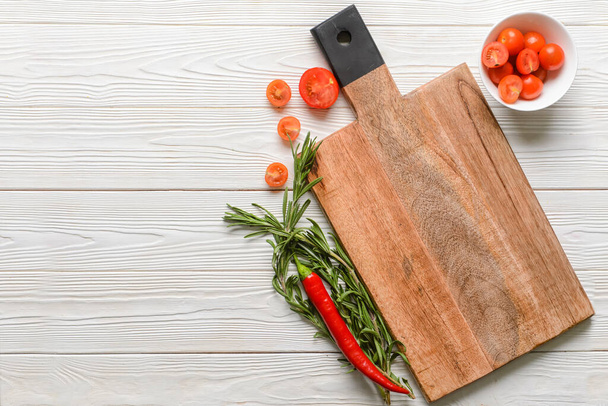 New cutting board with tomatoes, chili pepper and rosemary on light wooden background - Photo, Image