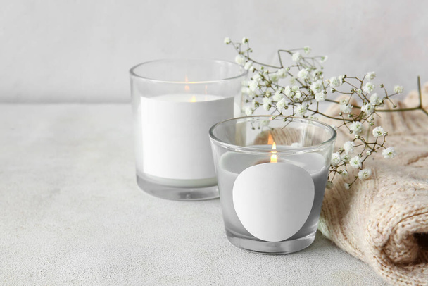 Glass holders with burning candles, flowers and sweater on light background, closeup - Фото, изображение