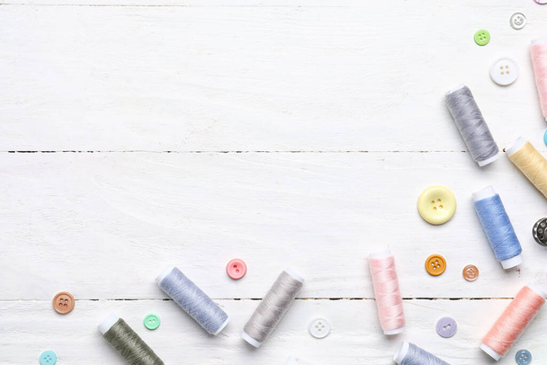Sewing threads with buttons on light wooden background - 写真・画像
