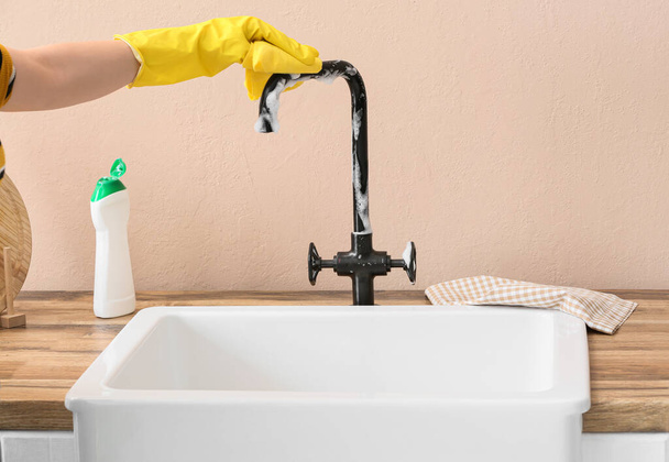 Woman in rubber glove cleaning faucet with sponge - Foto, afbeelding