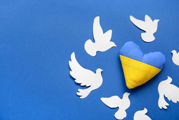 Corazón en colores de bandera ucraniana y palomas de papel como símbolo de paz sobre fondo azul - Foto, imagen