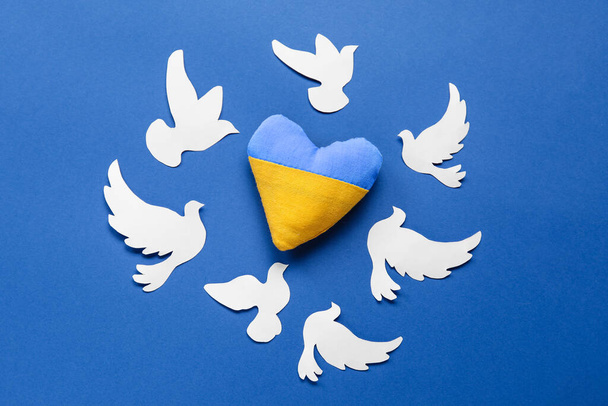 Серце в кольорах українського прапора і паперових голубів символізує мир на синьому тлі. - Фото, зображення