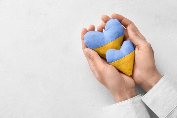 Hands with hearts in colors of Ukrainian flag on light background - Foto, imagen