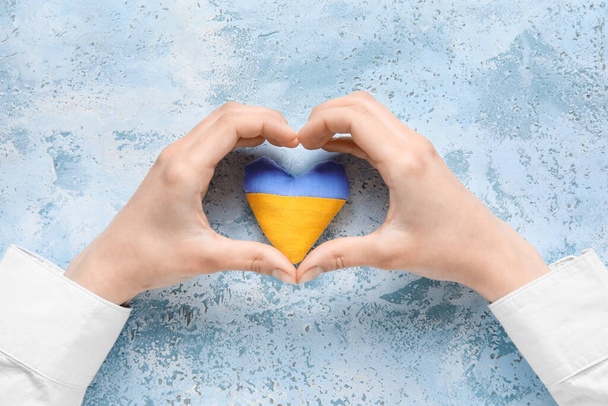 Hands with heart in colors of Ukrainian flag on light blue background - Foto, Imagen