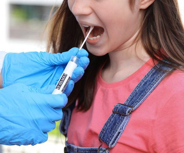 junges Mädchen während der Diagnose für die Coronavirus-Forschung mit einem oropharyngealen Abstrich und Handschuhen mit Reagenzglas - Foto, Bild