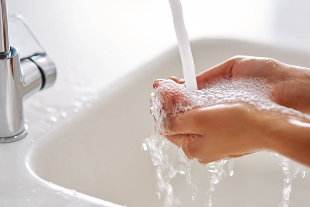 Bleiben Sie gesund, indem Sie sich die Hände waschen. Abgeschnittene Aufnahme von Händen, die an einem Wasserhahn gewaschen werden. - Foto, Bild