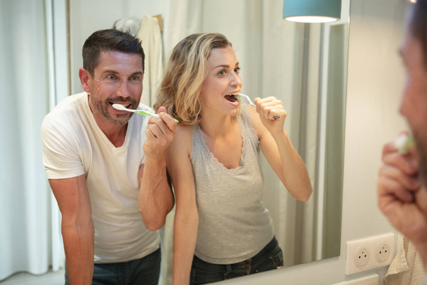 happy couple bonding while brushing teeth in the bathroom - Foto, afbeelding