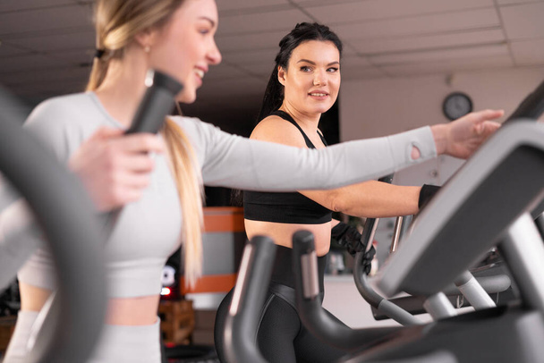 dos atractivas mujeres jóvenes atléticas están entrenando juntas en el gimnasio. Realizar ejercicio en la máquina cardiovascular. - Foto, imagen