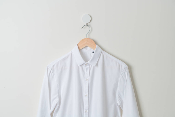 на стене висит белая рубашка с деревянной вешалкой - Фото, изображение