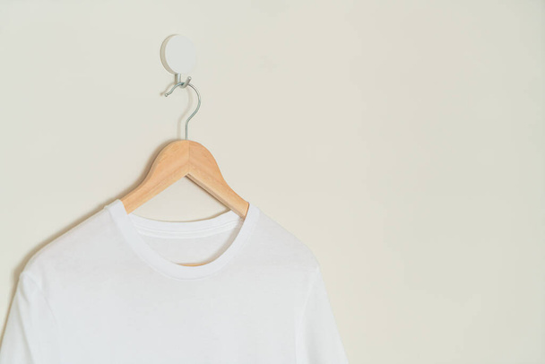 white t-shirt hanging with wood hanger on wall - Foto, immagini
