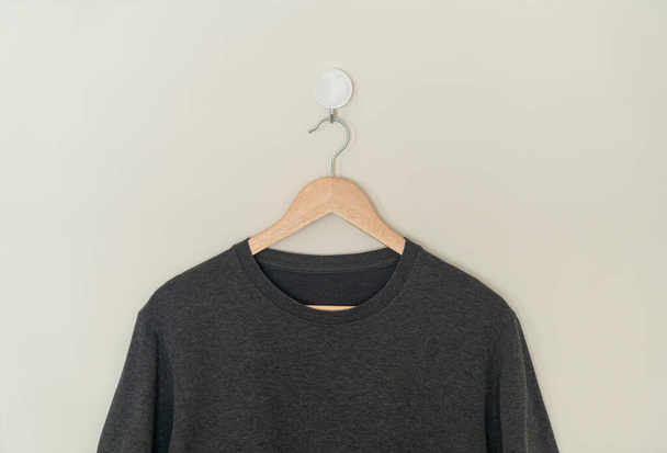 black t-shirt hanging with wood hanger on wall - Фото, зображення