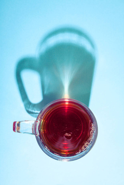 Glass of tea on blue background under the bright sunlight with creative shadow. - Photo, image