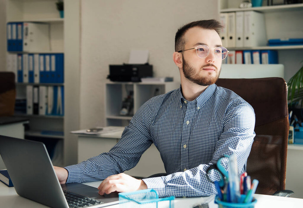 Jeune homme d'affaires en chemise travaillant sur son ordinateur portable dans un bureau - Photo, image