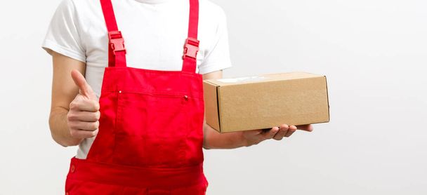 mage of a happy young delivery man in red cap standing with parcel post box isolated over white background. - 写真・画像