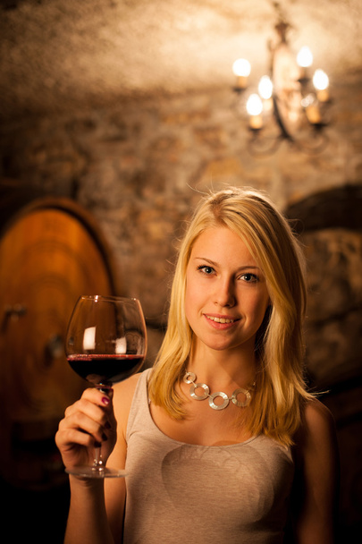Beautiful young blond woman tasting red wine in a wine cellar - Zdjęcie, obraz