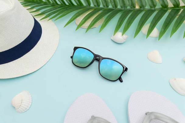 Summer beach accessories on blue background. Hat, glasses, slippers, shells and palm leaves - Фото, изображение