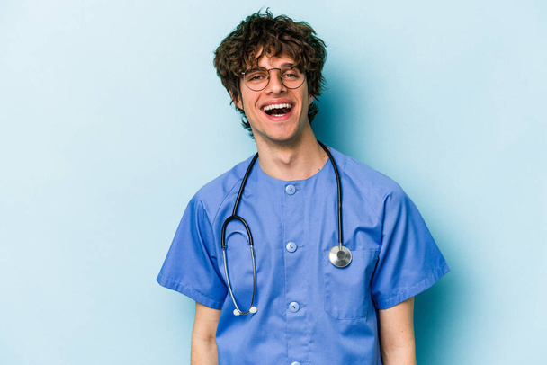 Nuori valkoihoinen sairaanhoitaja mies eristetty sinisellä taustalla onnellinen, hymyilevä ja iloinen. - Valokuva, kuva